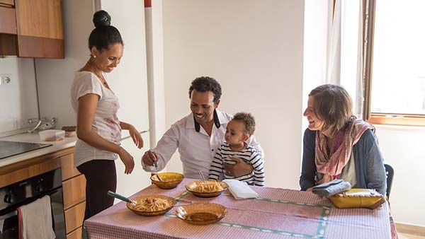 A family of four smiles while eating a meal at a kitchen table.