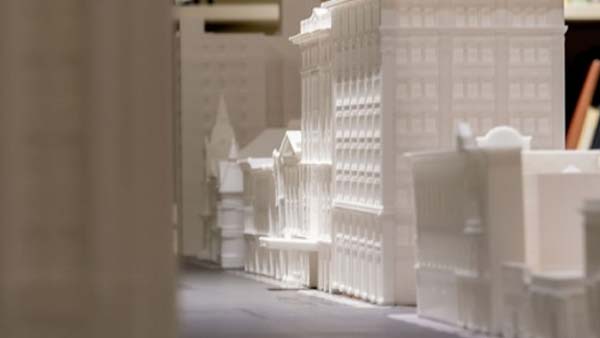 A close-up of a 3D-printed model of several white buildings, including one that resembles a church, with a blurred foreground.
