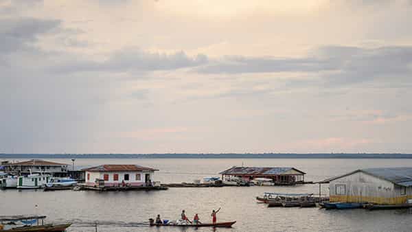 A small wooden boat carries several people and bags across a lake dotted with small floating houses under a cloudy sky.