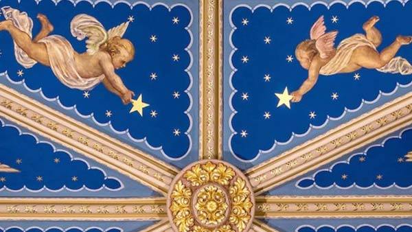 A detailed painting of two angels reaching for stars on a deep blue ceiling with gold accents.