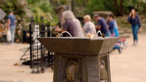 A close-up of a bronze fountain with water spouting from a central spout, and people are out of focus in the background.