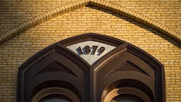 A close-up of a decorative arch above a window on a brick building with the number '1879' in the center.
