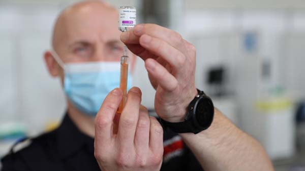 A healthcare worker in a blue surgical mask draws liquid from a vial into a syringe.