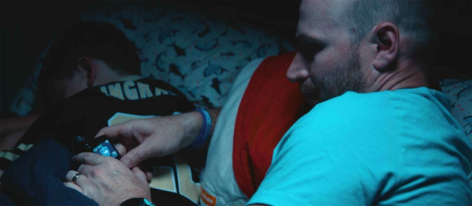 A father checks his son's glucose monitor while he sleeps beside him.