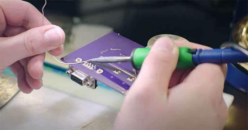 A close up of hands working on a circuit board.