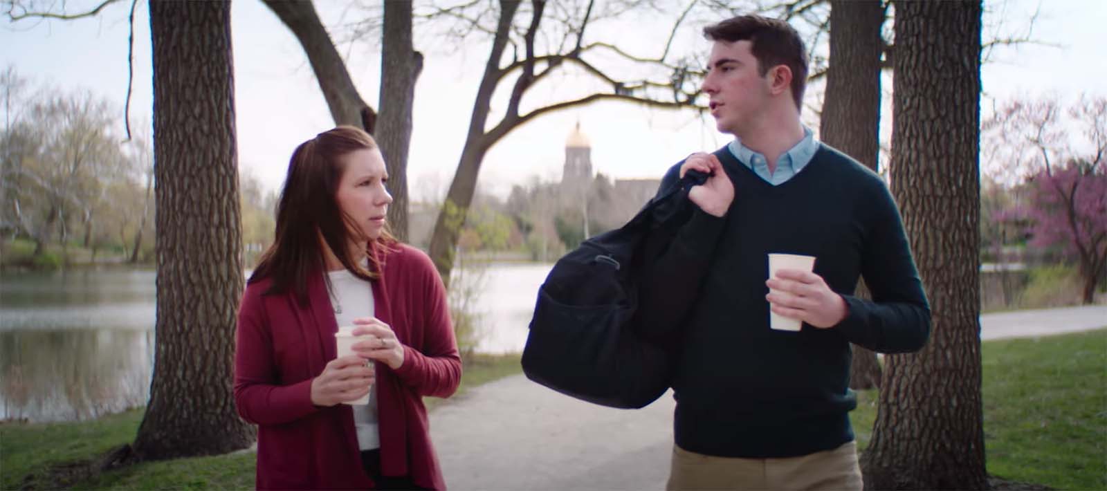 Two people walk by the lakes on Notre Dame's campus. The main building is in the distance.