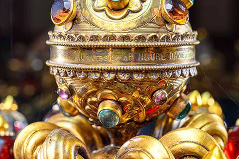 A close-up of a gold chalice with 'UNIVERSITY OF NOTRE DAME' engraved around the middle and a variety of colorful gems.