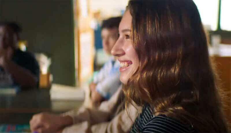 A girl smiles in a classroom.