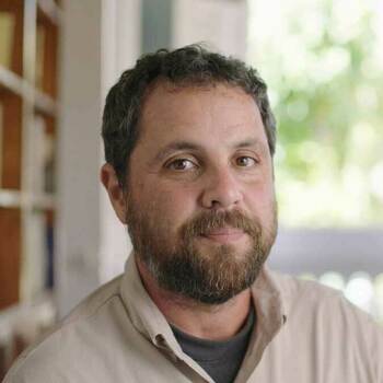 Associate professor, Matt Webber wearing a gray suit, blue shirt, and black tie.