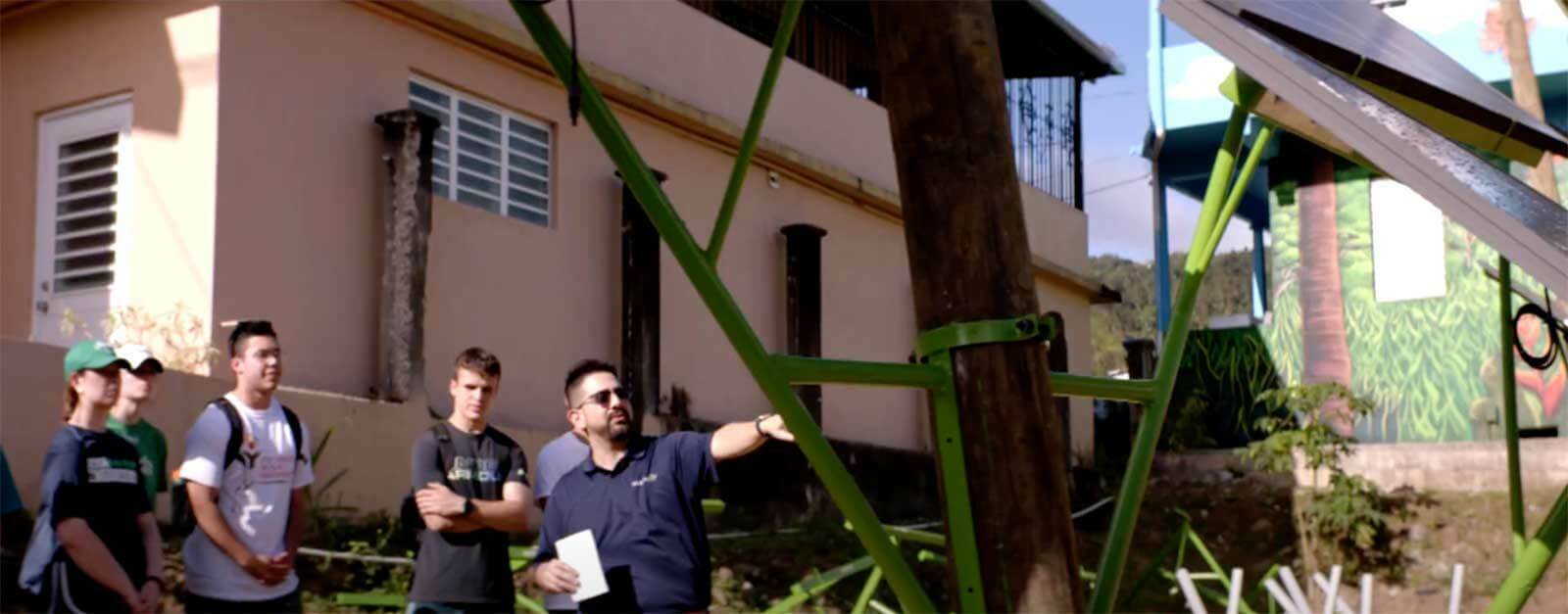 A man points at solar panels while talking to a group of students.