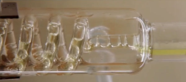 Horizontal glass tube with spiral glass tubing inside. The spiral tube has clear liquid flowing through.