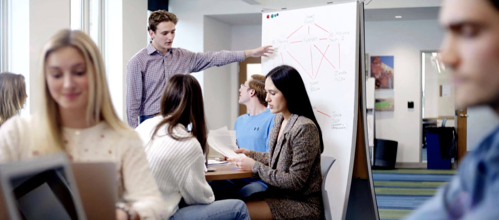 Greg Miller stands at a paper presentation board and talks with fellow students