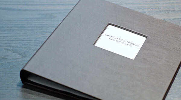 Black binder on a table with the label Student Policy Network Dos Santos file