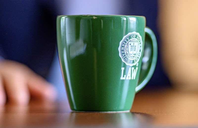 A close-up shot of a green mug with the University of Notre Dame Law logo on a wooden table.