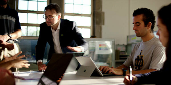 A male in glasses talks to a group of students at a desk.
