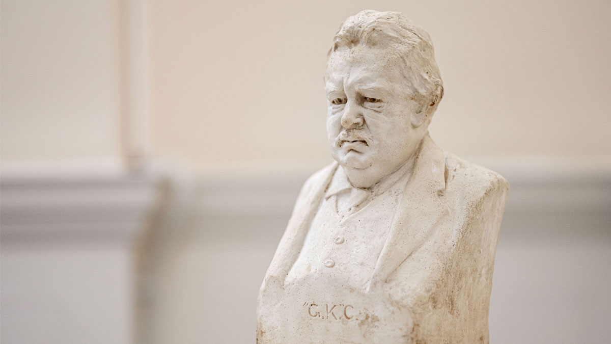 A stone bust of G.K. Chesterton looking slightly down and to the side. The letters 'G.K.C.' are carved into the front.