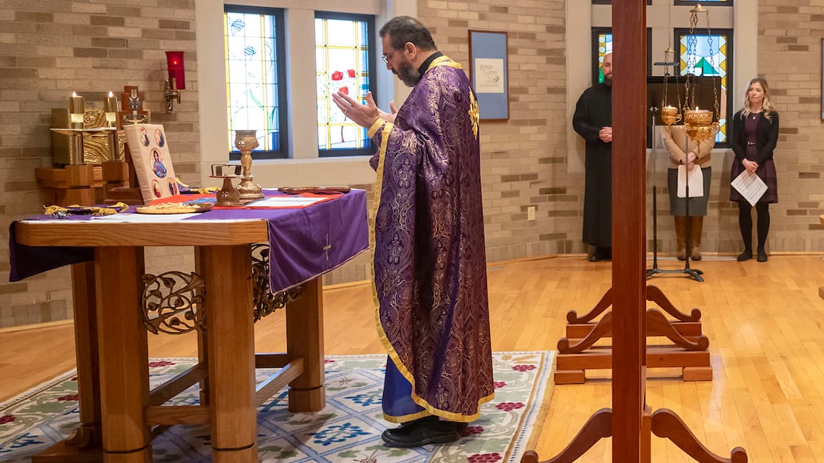 Fr. Khaled Anatolios wears a purple vestment. He stands facing an alter while performing a Byzantine Mass.