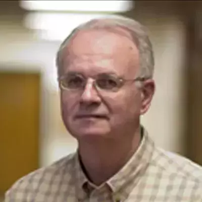 A white man with short gray hair and glasses, wearing a light brown and white plaid shirt.