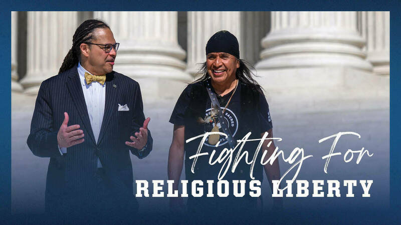 A black man and a Native American man walk and talk in front of a building with large columns. Text overlaid on the image reads "Fighting For Religious Liberty".