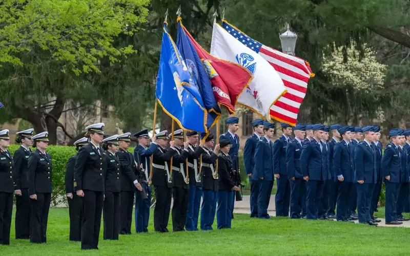 Members of the Notre Dame ROTC stand in formation on a grassy area. They flank flag bearers holding the U.S. flag, the Indiana state flag, and military branch flags.