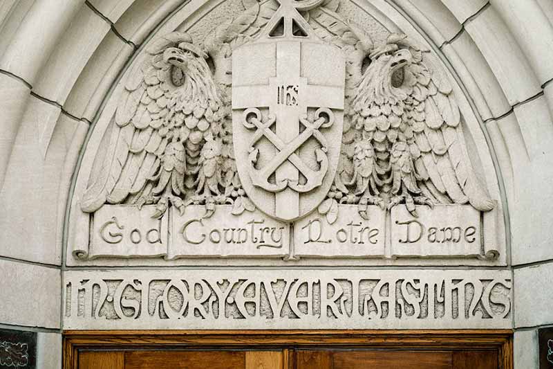 A stone carving above a doorway with the words, &lsquo;God, Country, Notre Dame&rsquoi; flanked by two eagle-like figures. 
