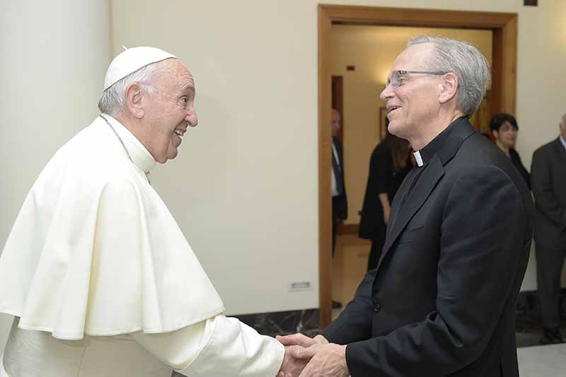 Pope Francis, smiling and wearing white, shakes hands with Father John Jenkins. 