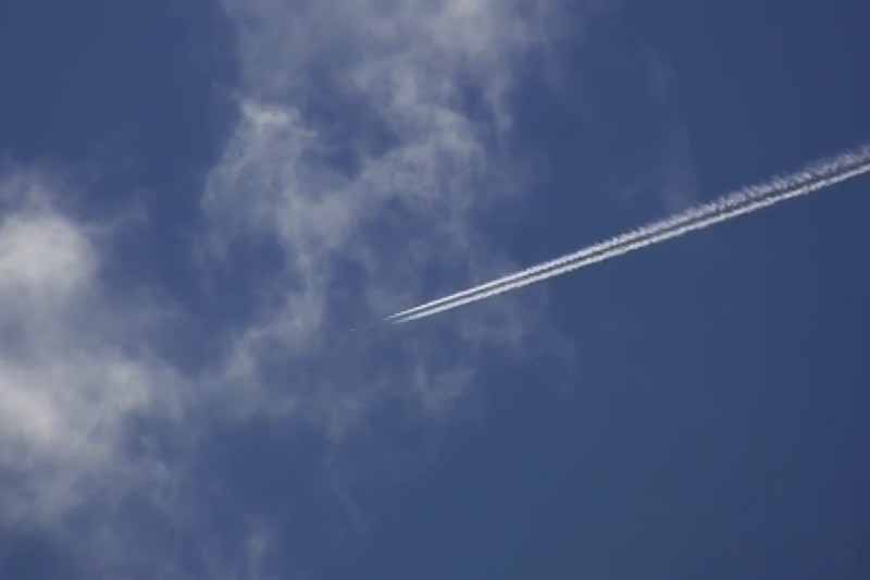 A contrail from an airplane stretches across a blue sky with white clouds. 