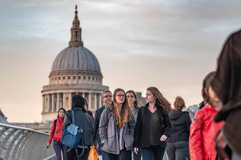 A group of people walk along a bridge in London with St. Paul's Cathedral visible in the background. 