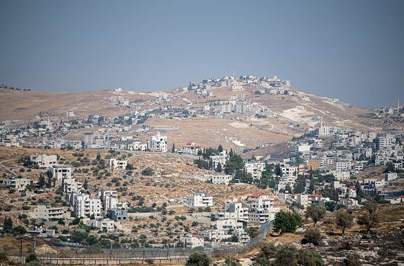 A wide view of a city with many light-colored buildings climbing up a brown, rocky hillside. 