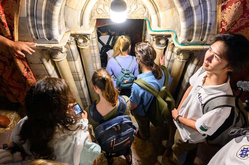 People crouch to enter a low, ornately decorated arched doorway into the Grotto of the Nativity. 