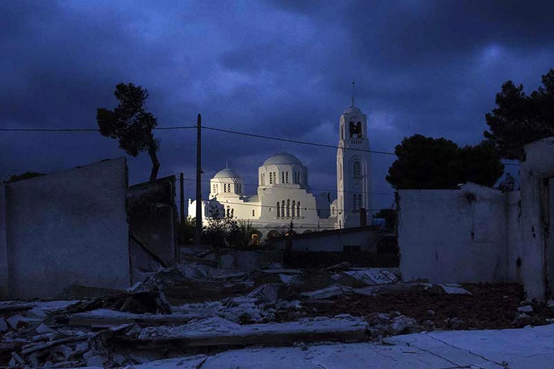 An illuminated white church with a large dome and a bell tower is surrounded by debris at night. 