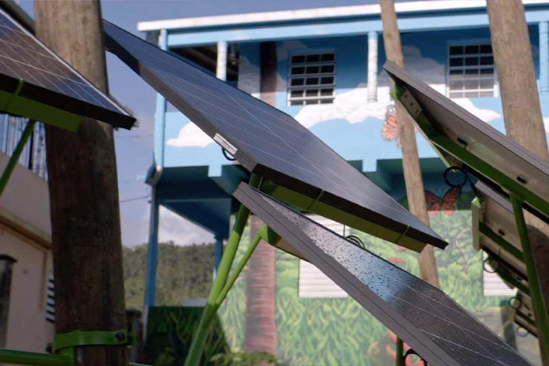 Several solar panels angled upwards, with a blue building featuring a mural of trees and a butterfly in the background.