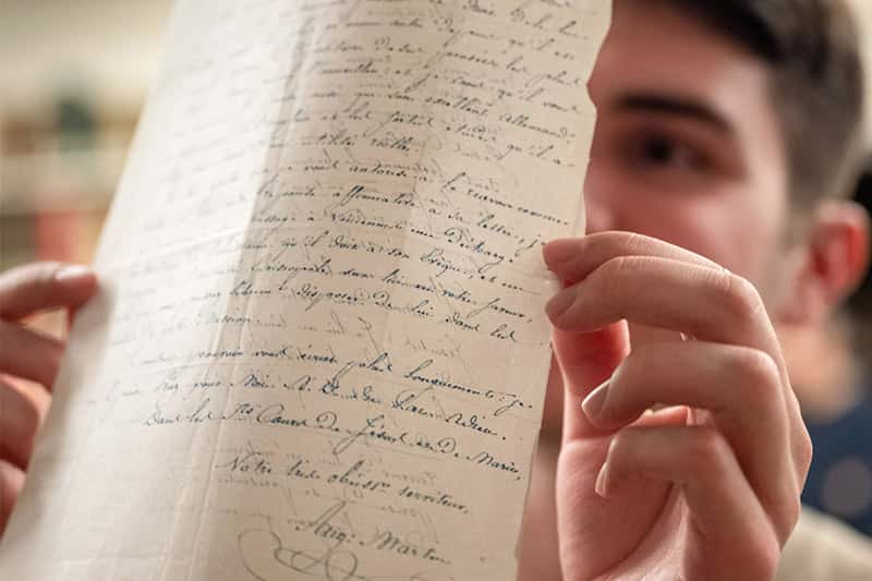 A man holds up a document with handwritten cursive text, partially obscuring his face.
