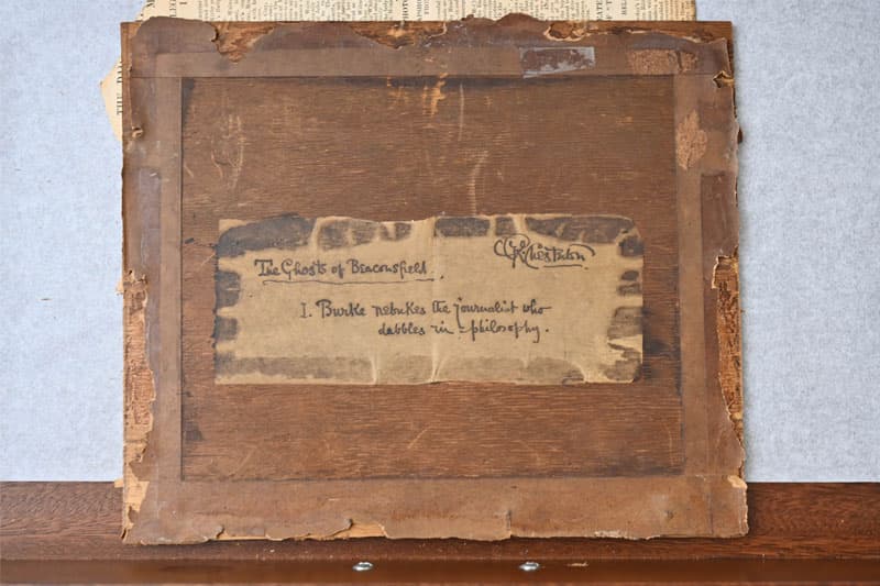 Wooden back of a framed picture with a partial label reading The Ghosts of Beaconsfield. and I. Burke rebukes the journalist who dabbles in philosophy. A signature is visible above the text.
