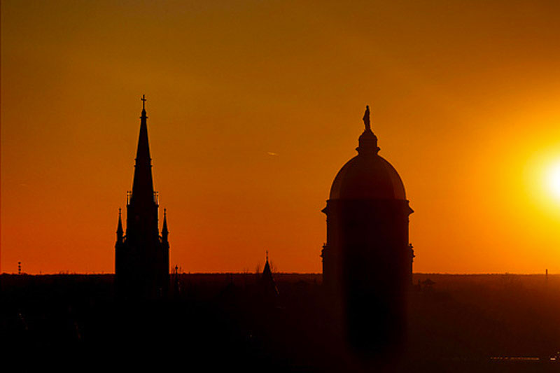 A beautiful silhouette of the Golden Dome and Basilica against a vibrant orange and yellow sunset.