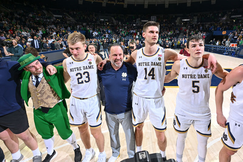 A group of Notre Dame men's basketball players and their coach on a basketball court, presumably after a game.