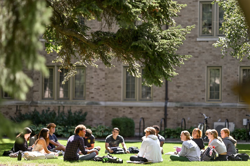 A group of students sitting in a circle on a grassy lawn.