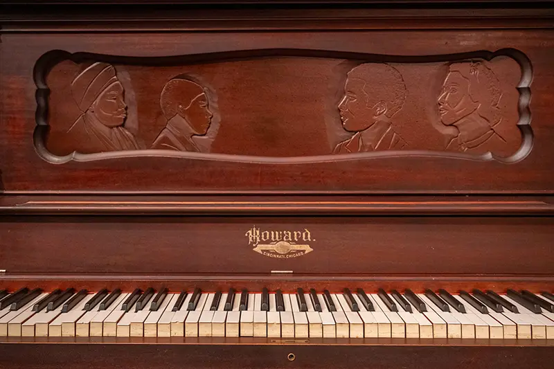 Front of piano with Howard nameplate and 4 busts of people facing inward.
