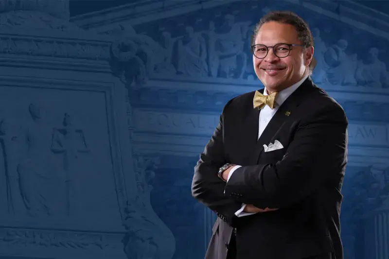 Black Man in pinstripe suit and gold bow tie against a blue background.