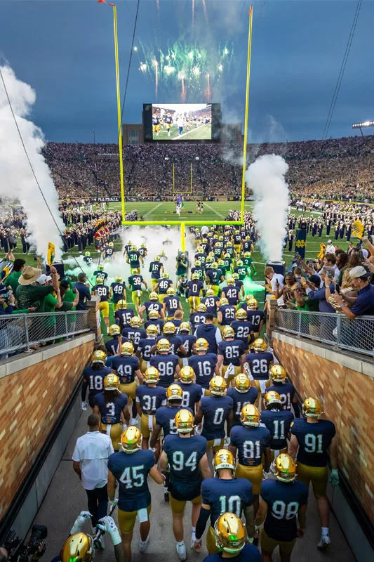 erial view of Notre Dame Stadium filled with fans during a performance. Four helicopters fly over the green field where the Band of the Fighting Irish forms the ND logo.