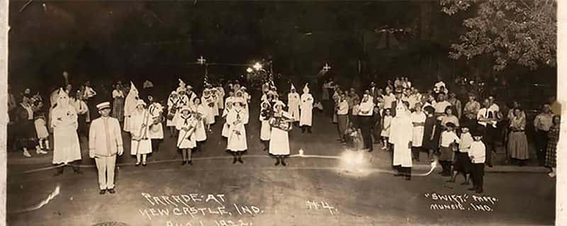 A parade of men in Klan robes and women playing instruments stand at attention in Newcastle, Indiana in 1922.