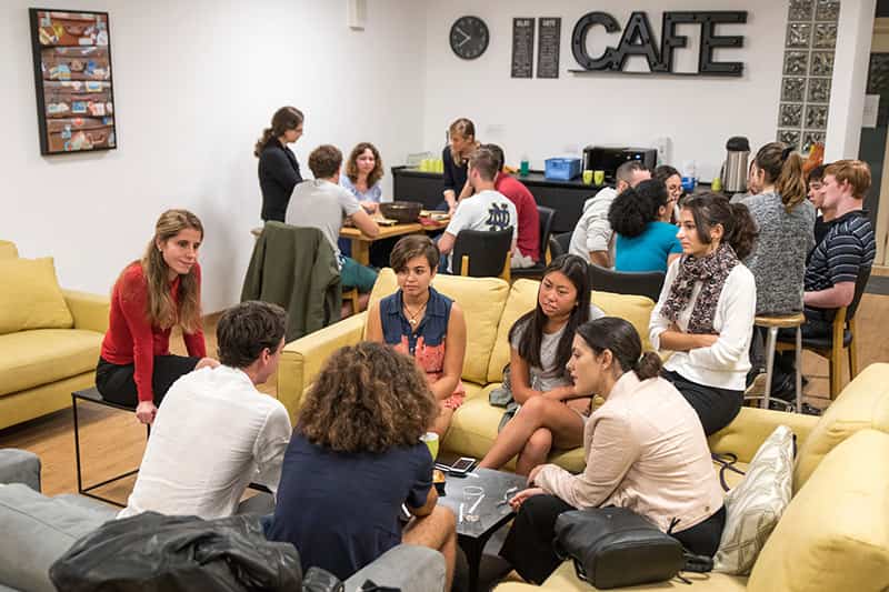 Students sit at tables and couches talking to one another.