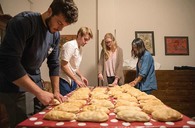 Four students prepare panini's at a table.