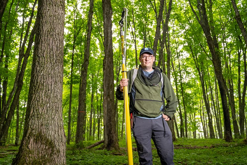 A man holding a pole saw standing in a forest