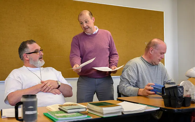 Brian O'Conchubhair stands in between two students who are seated at a table.