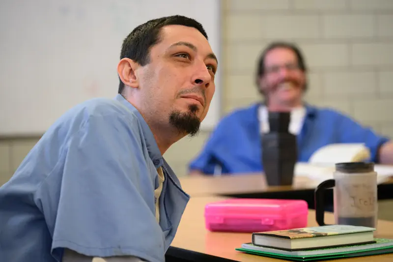 A male prisoner sits in a classroom listening to the professor, who is out of the frame.