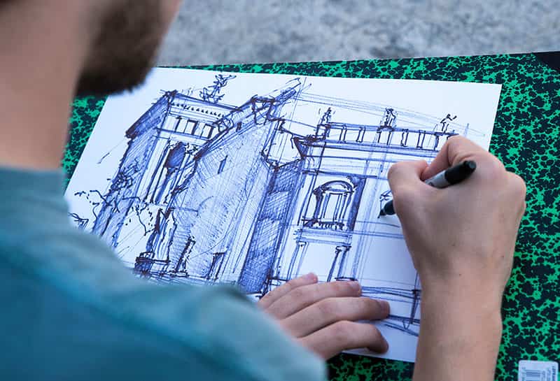 An over the shoulder shot of a student tracing their sketch with permanent marker.