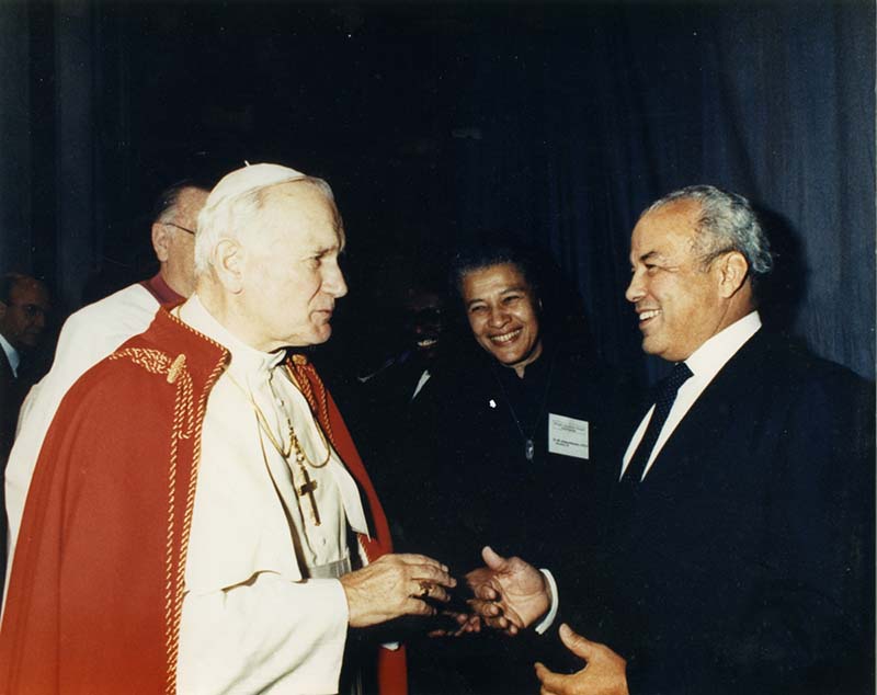 Pope John Paul II wearing red and white vestments shakes the hand of Norman Francis.