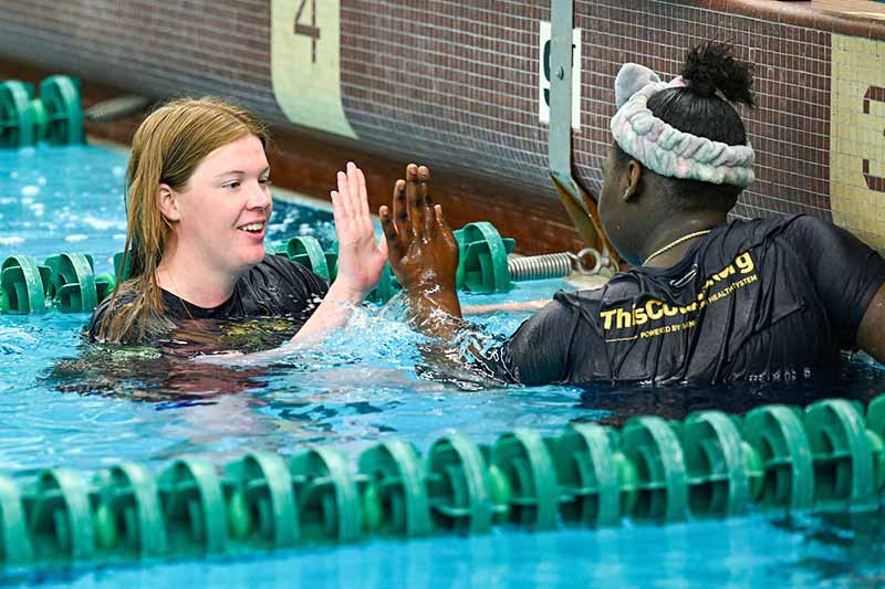 A student athlete and a middle schooler give each other a high five in a swim lane.