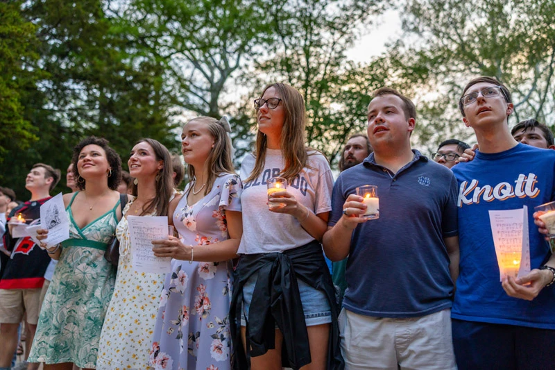 Notre Dame students hold lit candles and song sheets during an outdoor evening vigil.